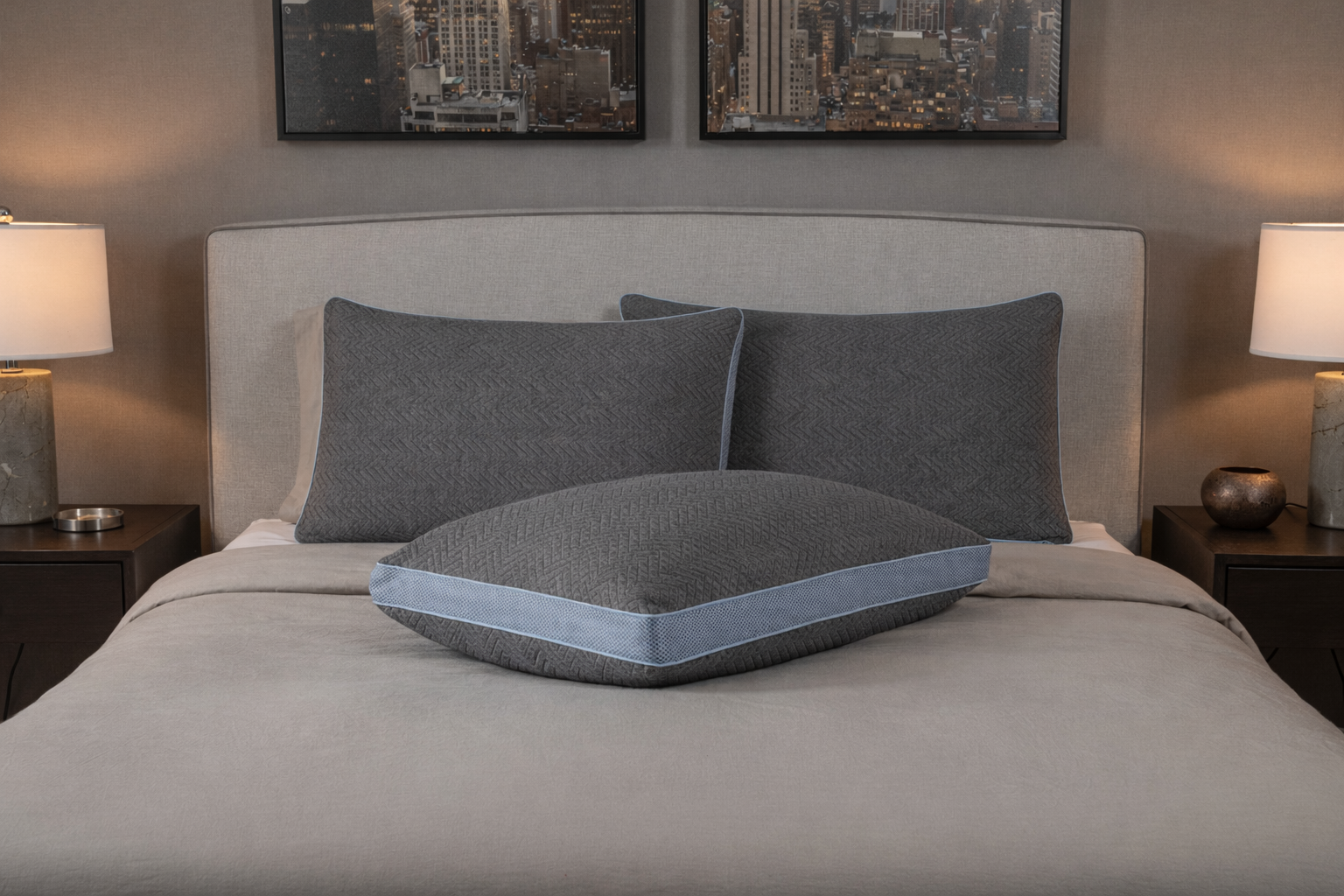 Gray pillow on a bed in a bedroom setting with lamps and wall art.
